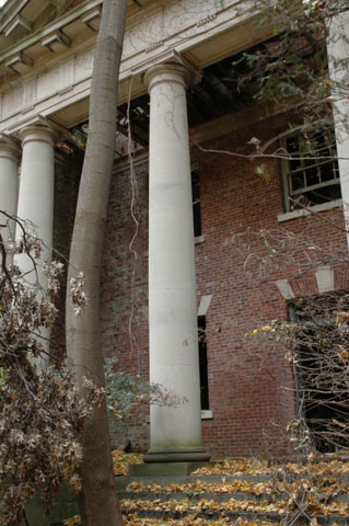 <p><strong>Neoclassical, details</strong>: Doric design elements, plain columns, and elaborated doorway, Administration Building (Building 13), center pavilion, or portico. East facade, view northwest, November 2005.</p>