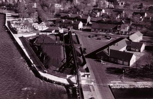 <p>Aerial view of a portion of the Quartermaster Area and adjoining areas, looking northeast, taken in November 1961. The Coal Yard (Building 27A)&#160; and part of the conveyor system is in the left foreground, and the Garage (Building 40) is in the right foreground. The small, 1950s-era trailer park at Fort Slocum can be seen to the left of the Coal Yard.</p>