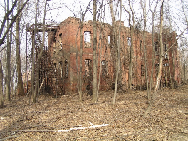 <p>View north-northeast of the front west wing of the main Hospital (Building 46), taken in March 2006. The wood porch in front of the brick wall was destroyed when the building was destroyed by fire in April 1982. The building was demolished in June 2008.</p>