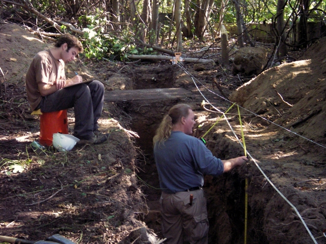<p>To record information revealed during archeological testing, two members of the field team prepare a measured drawing of soil layers in a trench near the foundation of Building 131 in the Defense and Support Area, October 2006.</p>